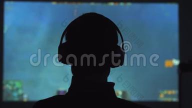 一个年轻人在黑暗的房间里玩电子游戏，用耳机看电影。 3840x2160
